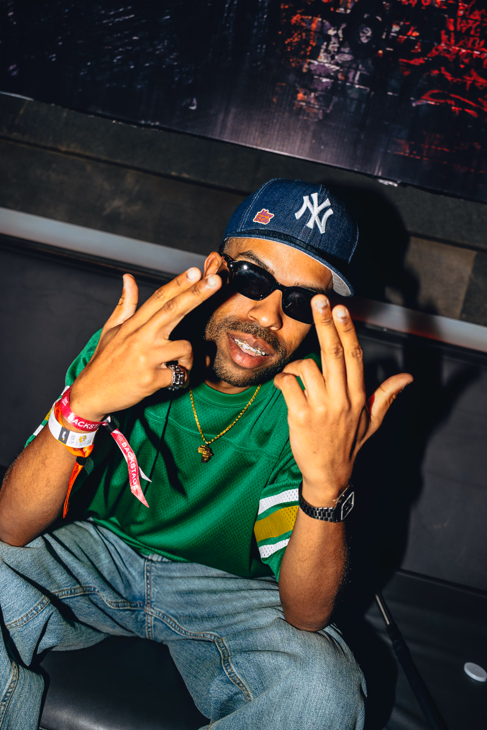 Seated guest in a green shirt and New York cap gesturing at the camera
